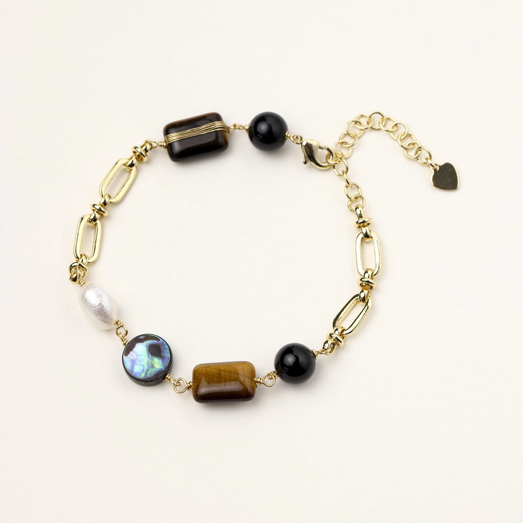 Gold chain bracelet with tiger's eye, obsidian, pearl, and iridescent abalone stones on cream background.