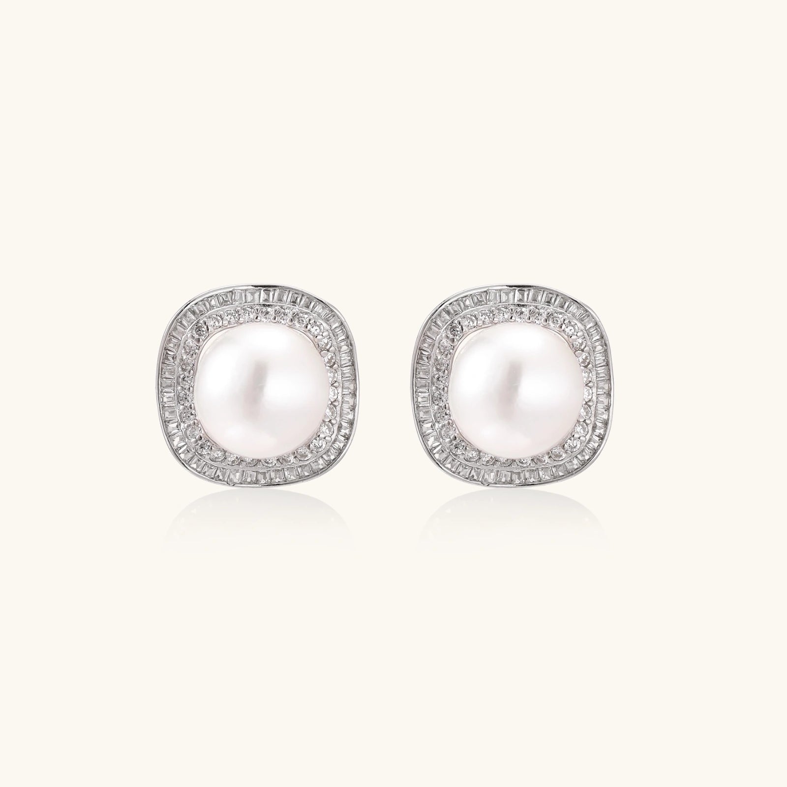 Rhodium-plated sterling silver stud earrings with round freshwater pearls surrounded by geometric crystal halos on cream background.