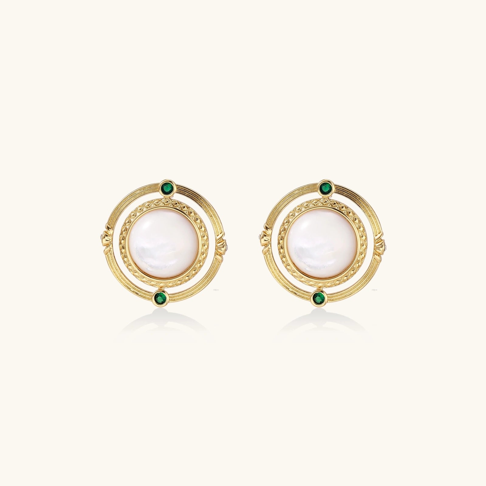 Circular gold stud earrings with iridescent mother-of-pearl center and green zirconia accents on cream background.