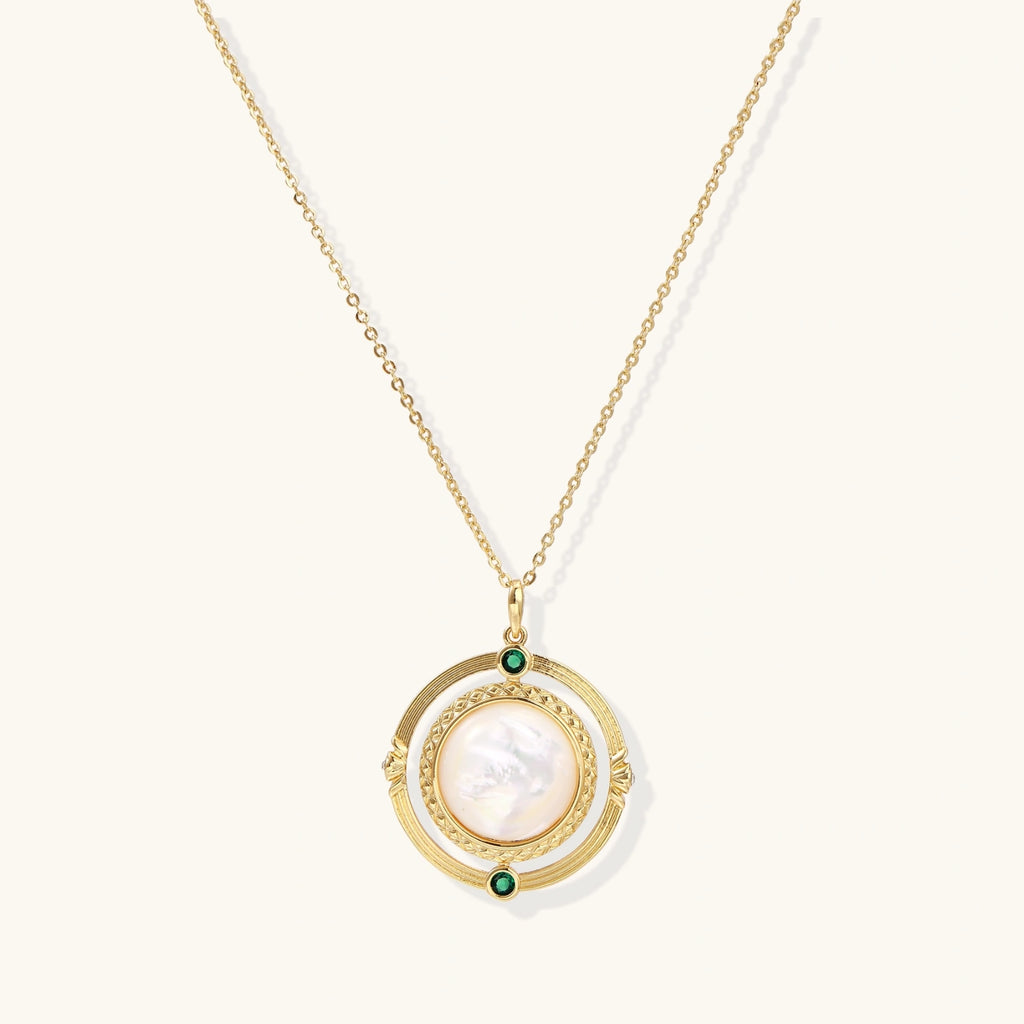 Gold pendant necklace with circular orbital design, iridescent mother-of-pearl center, and green zirconia accents