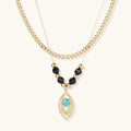 Layered gold necklace with turquoise evil eye pendant and black quartz beads on cream background