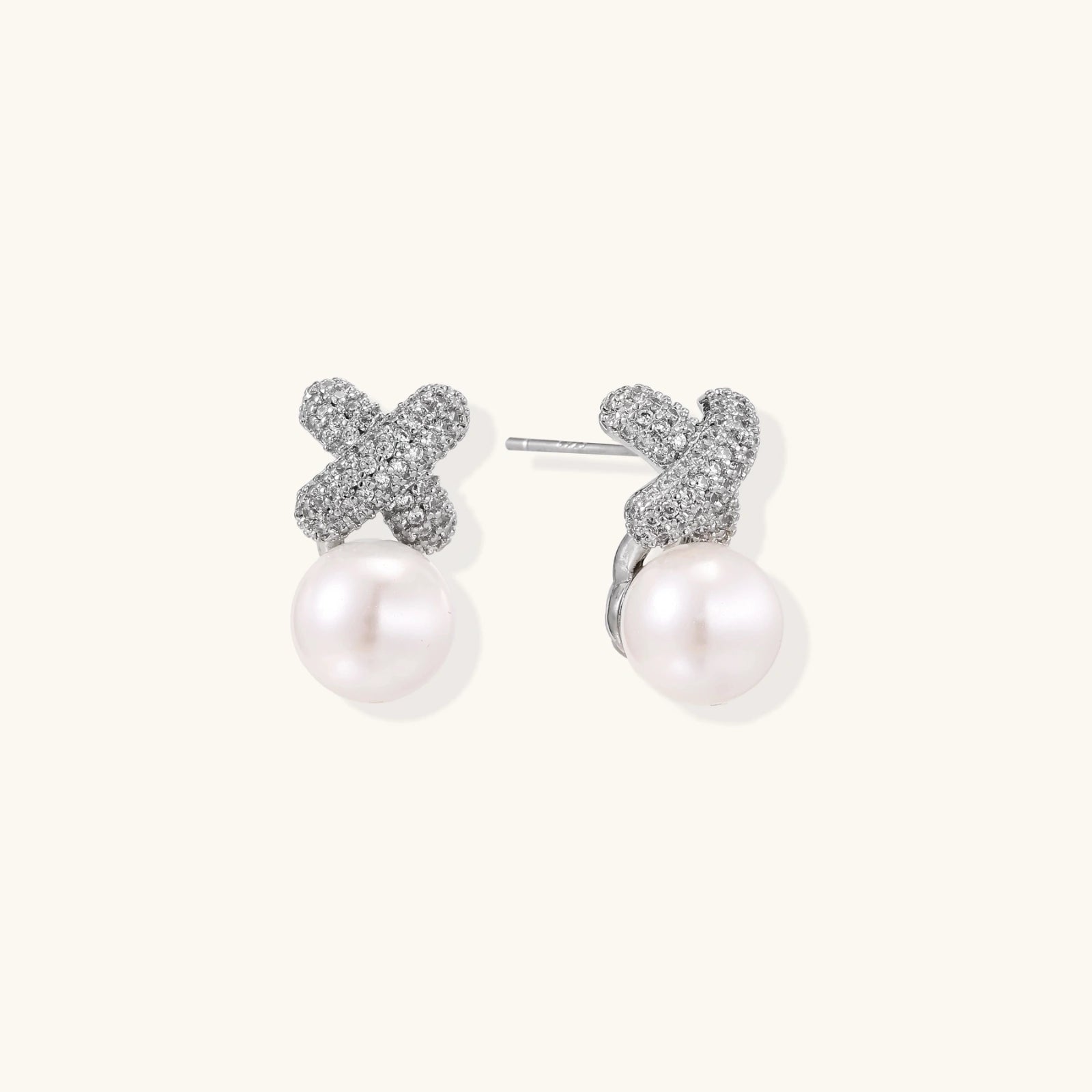 White gold plated studs featuring pavé X-shaped tops with freshwater pearl drops on cream background.